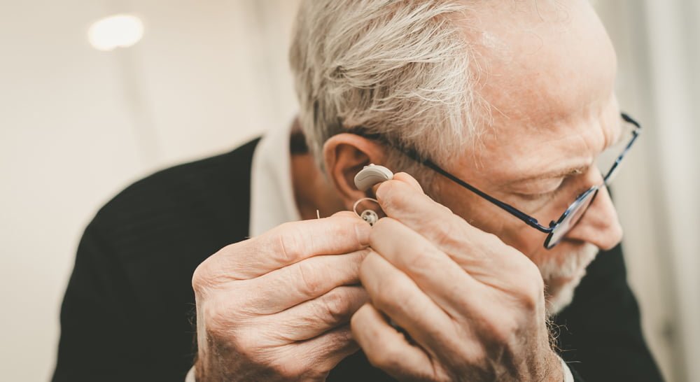 Elderly man putting on a hearing aid