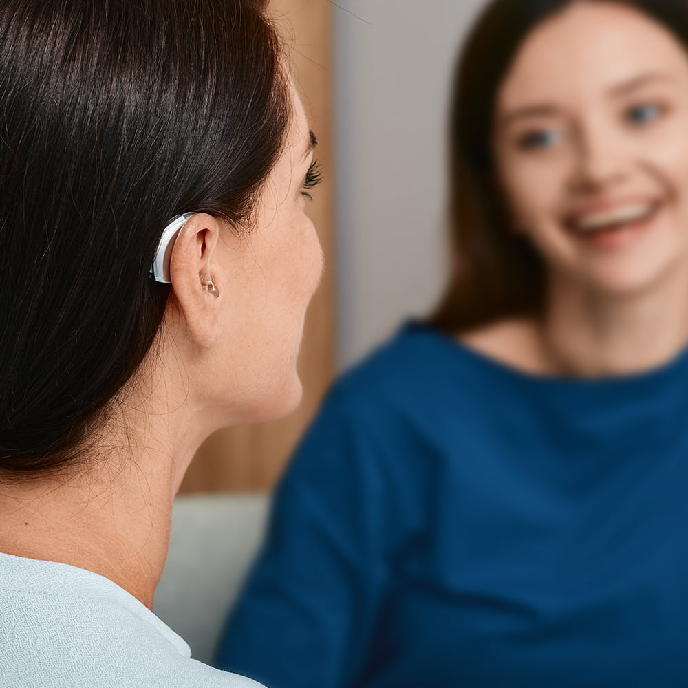 Young woman wearing hearing aid having conversation with friend