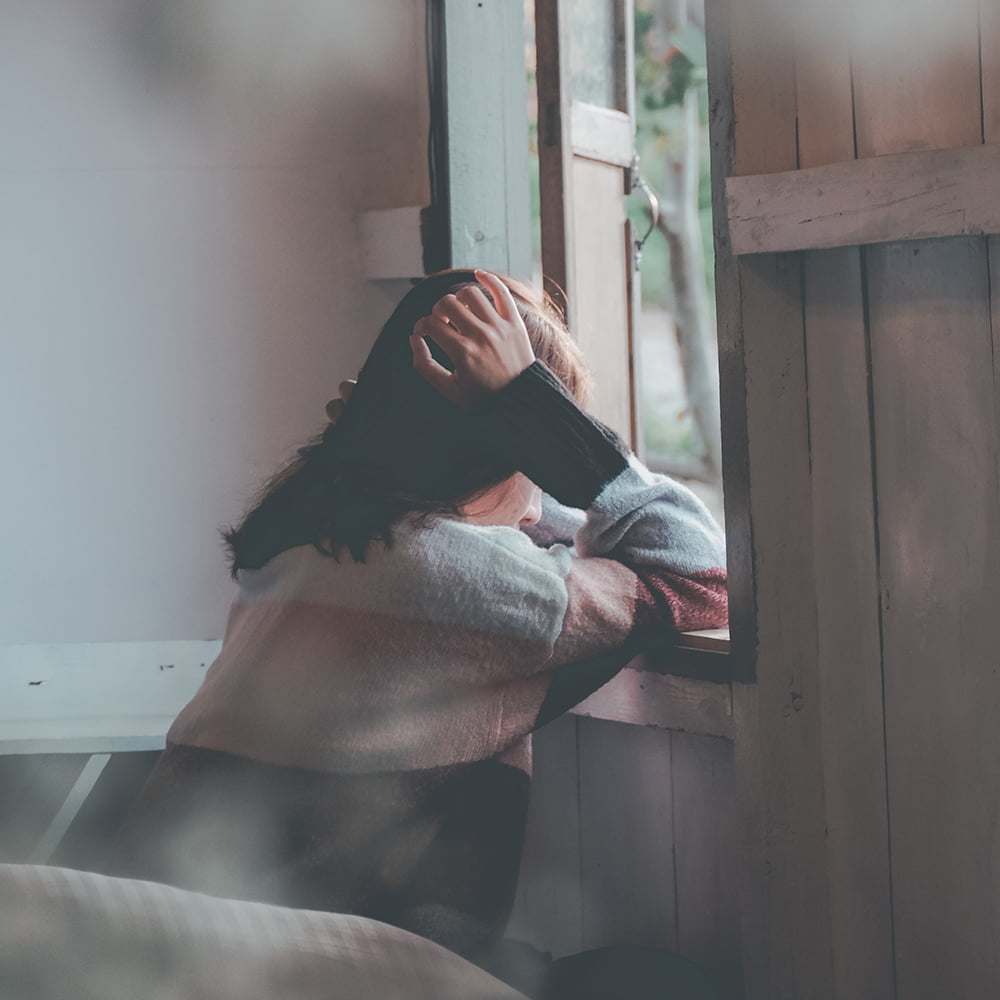 Young woman sitting by window seeming lonely