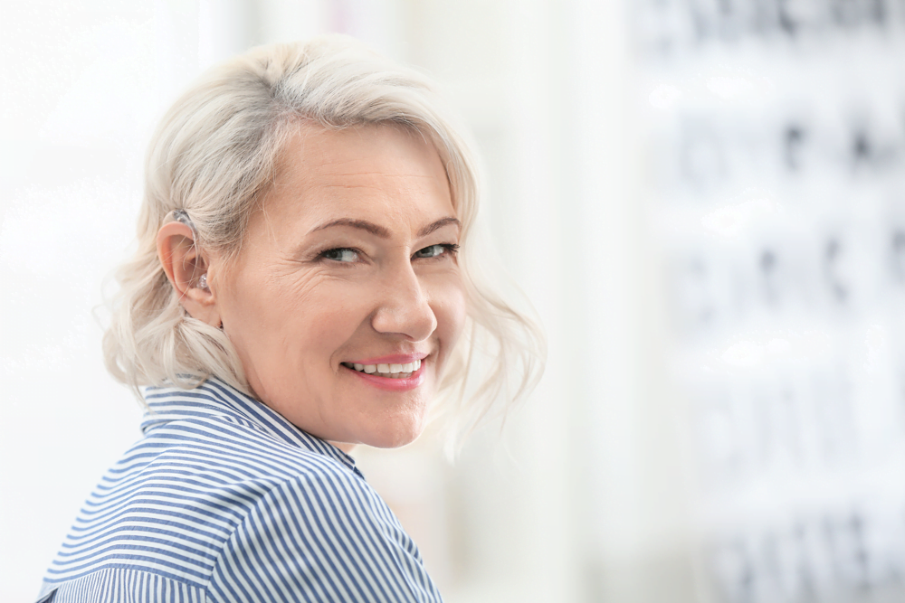 Elderly white-haired woman looking at camera, wearing a hearing aid, smiling