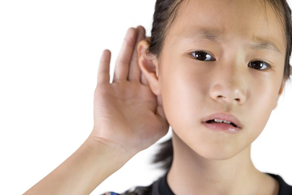 Young asian girl holding hand up to her ear, visibly struggling to hear