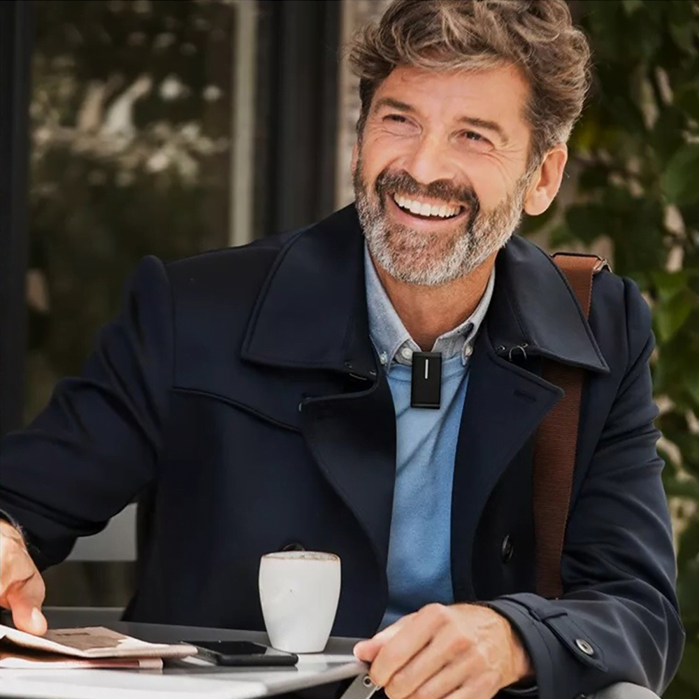 A senior man wearing a hearing aid microphone while sitting outside a cafe