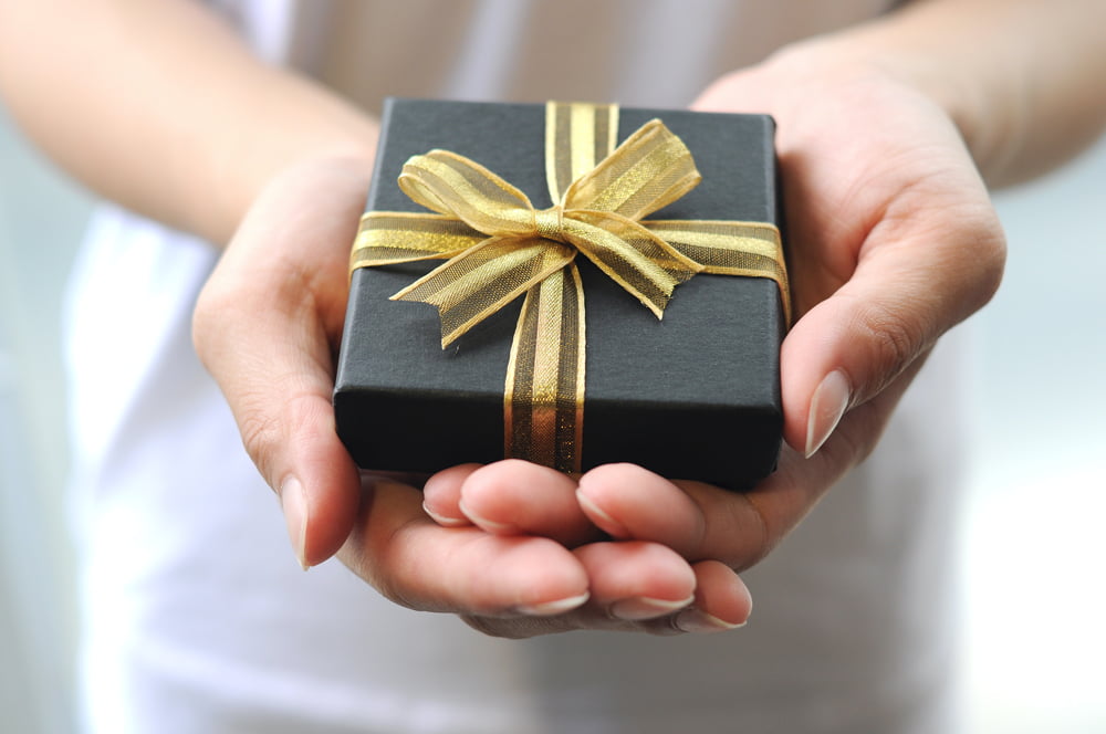 Closeup of hands holding a black gift box with golden ribbon