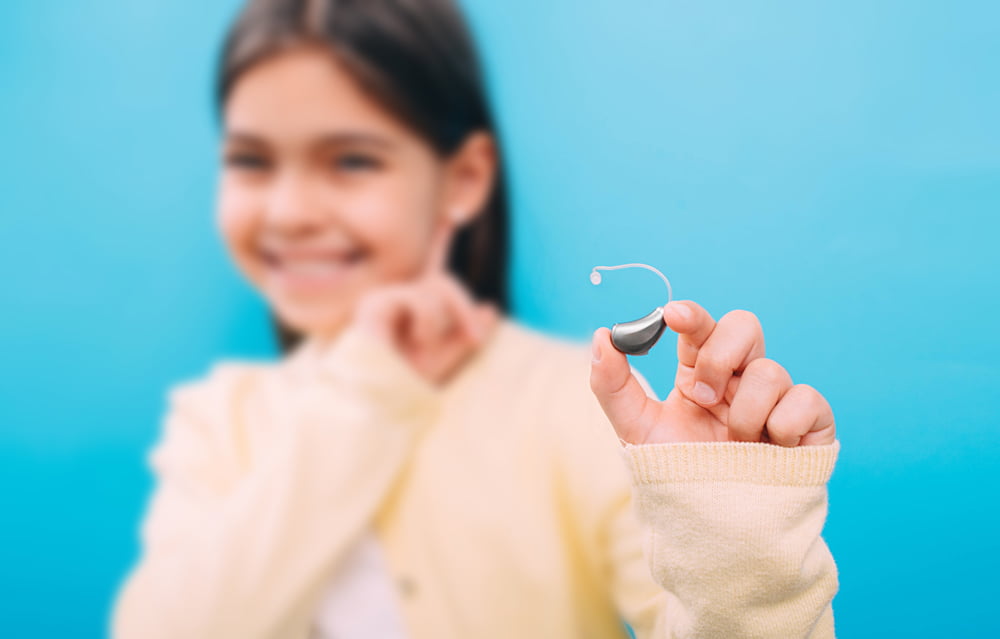 Smiling child holding a hearing aid