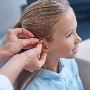 Doctor fitting hearing aid on young child's ear