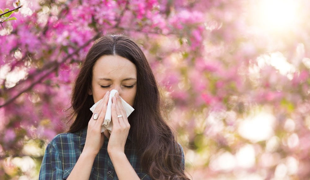 Young woman in park blowing nose, apparently suffering from pollen allergy