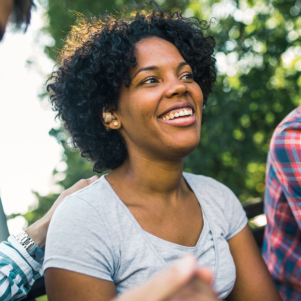 Young woman wearing a hearing aid with friends in park