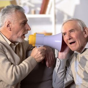 Middle-aged man using a megaphone to shout into the ear of hard-of-hearing conversation partner