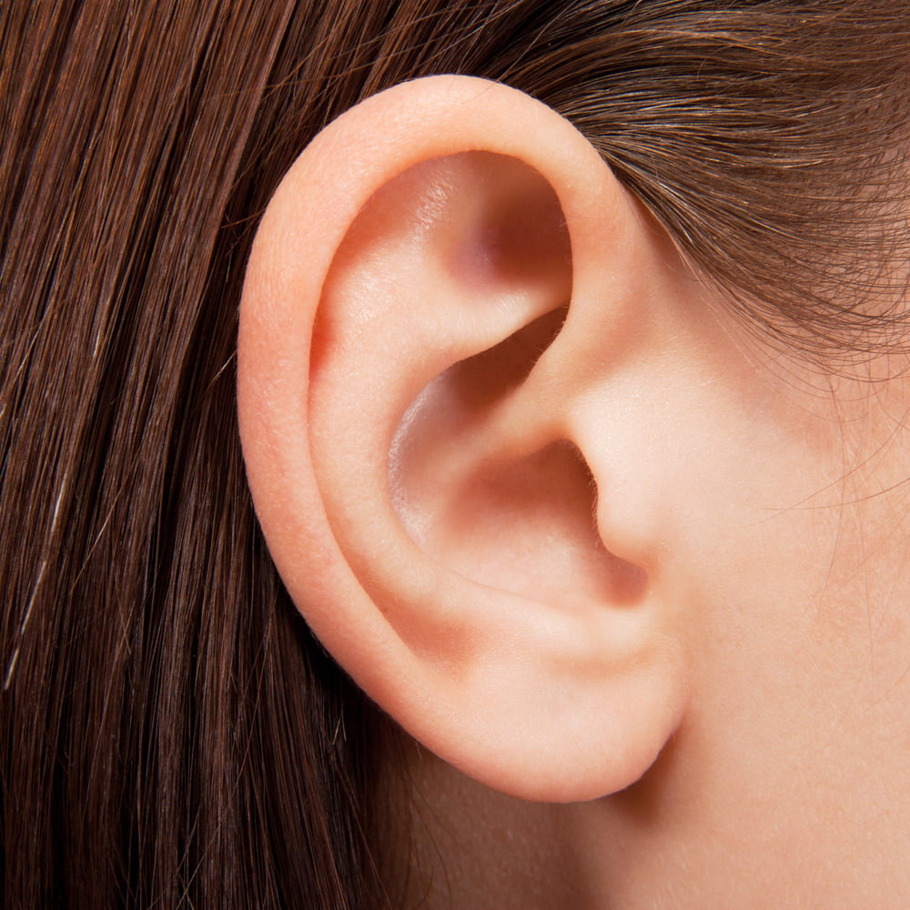 Closeup of ear with strands of brown hair tucked behind it.