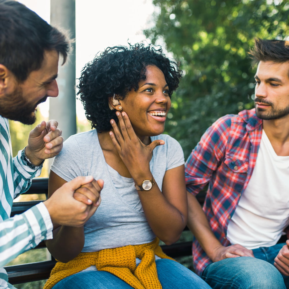 Young woman wearing a hearing aid socialising with friends outdoors.