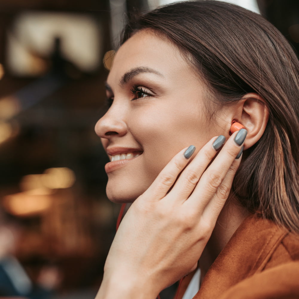 Woman with brown hair smiling, wearing bright orange earplugs