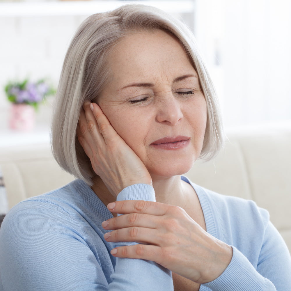 Senior woman holding right hand up to ear, visibly uncomfortable/in pain.