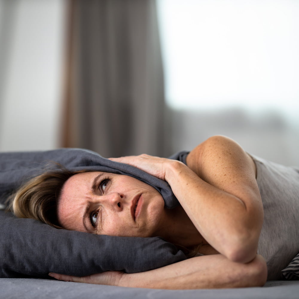 Middle-aged woman in bed, pressing both sides of pillow to ears